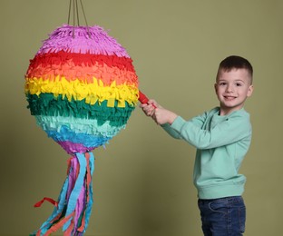 Happy boy breaking colorful pinata with stick on olive color background