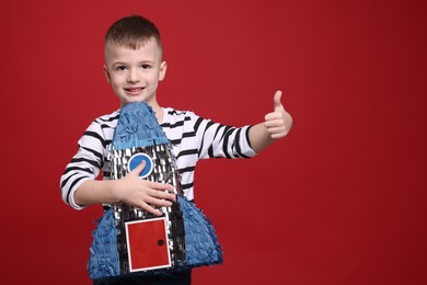 Happy boy with rocket shaped pinata showing thumbs up on red background. Space for text