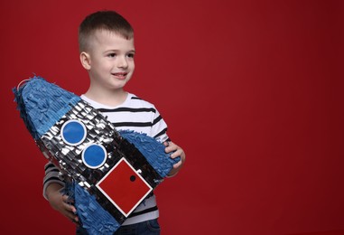 Happy boy with rocket shaped pinata on red background. Space for text