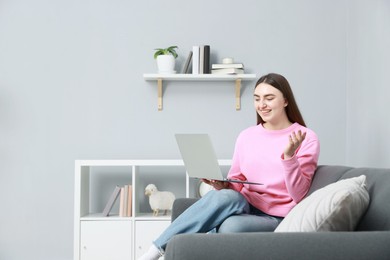 Photo of Happy young woman having video chat via laptop on sofa at home