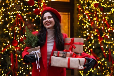 Photo of Happy woman with Christmas gifts and thuja tree on city street