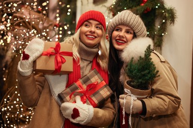 Happy friends with Christmas gifts and thuja tree on city street