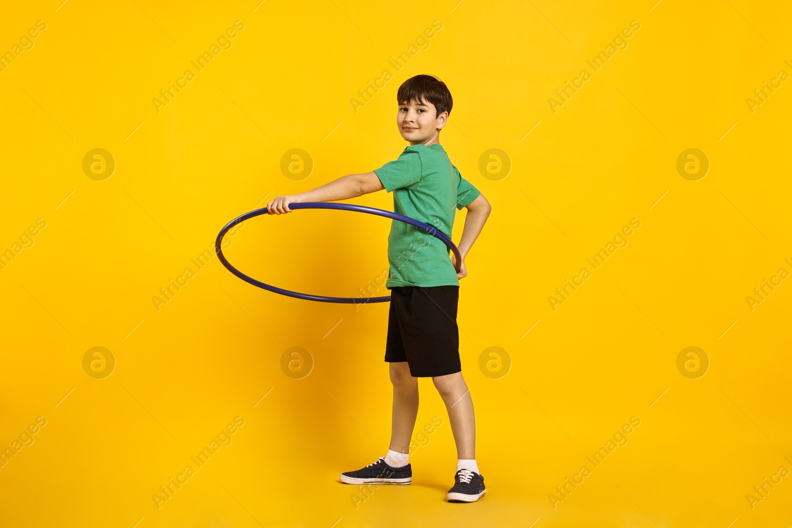 Photo of Boy exercising with hula hoop on yellow background