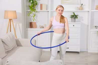 Beautiful young woman exercising with hula hoop at home