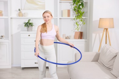 Photo of Beautiful young woman exercising with hula hoop at home