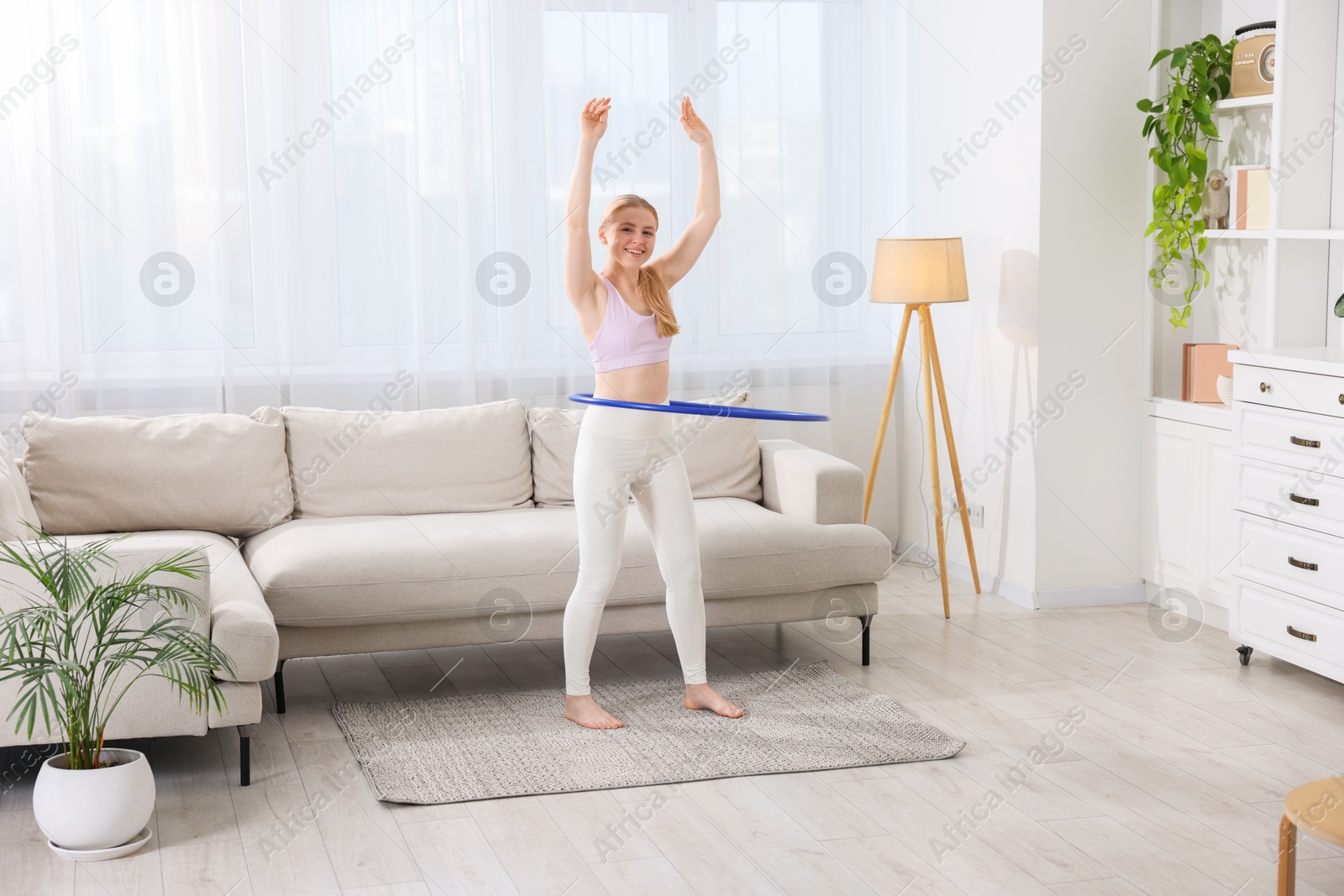 Photo of Beautiful young woman exercising with hula hoop at home