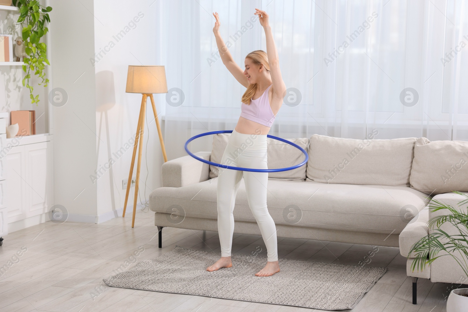 Photo of Beautiful young woman exercising with hula hoop at home