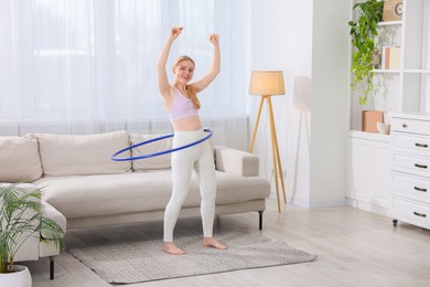 Beautiful young woman exercising with hula hoop at home