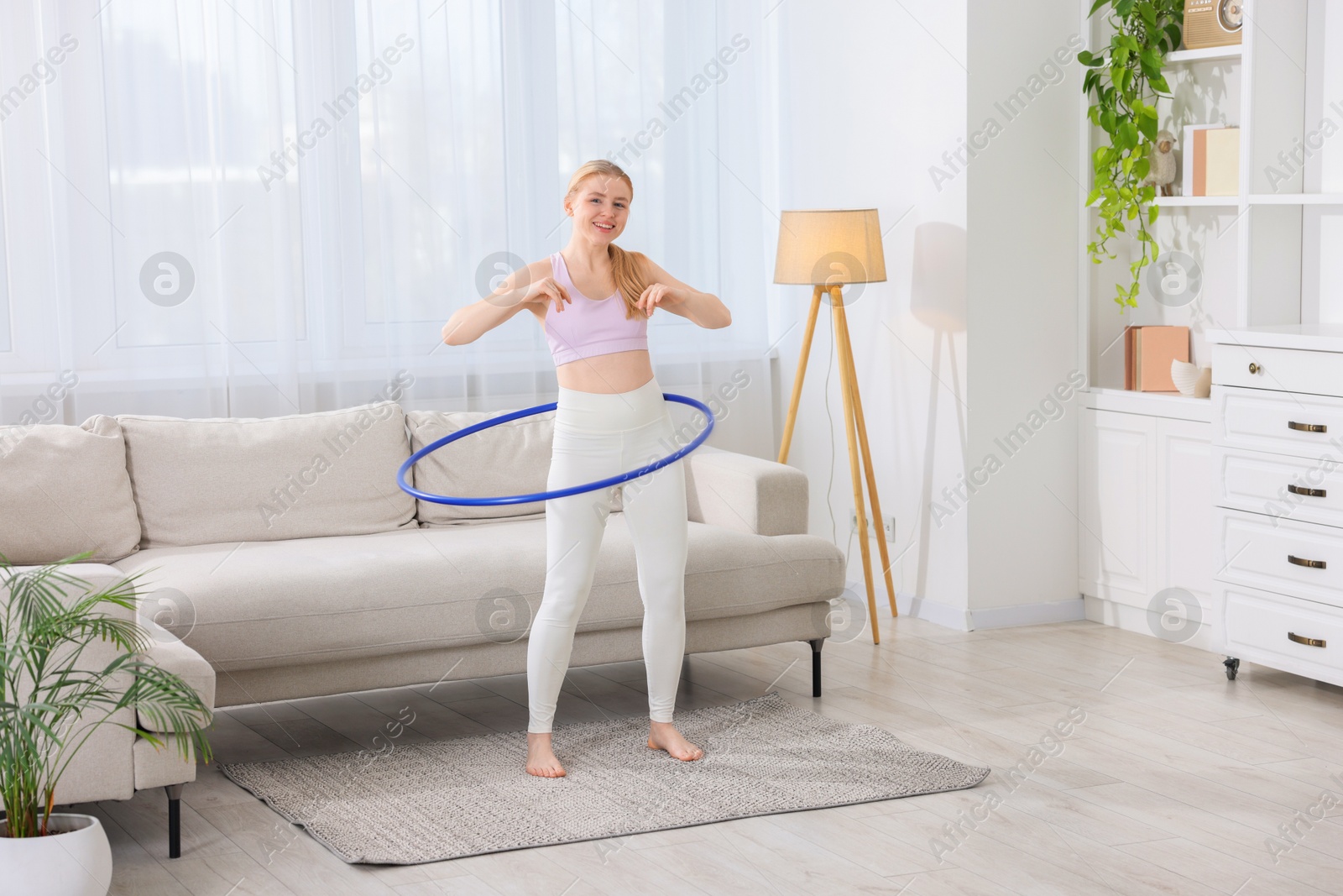 Photo of Beautiful young woman exercising with hula hoop at home