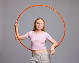 Beautiful young woman with hula hoop on grey background