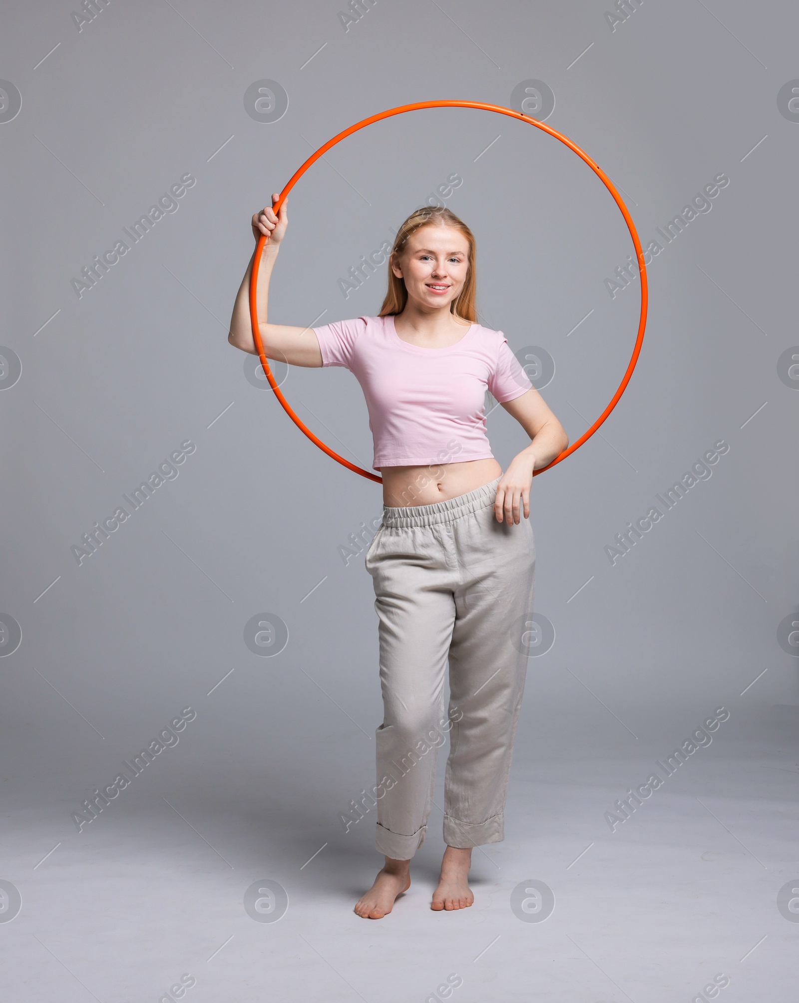 Photo of Beautiful young woman with hula hoop on grey background