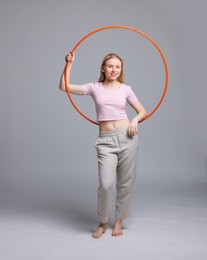 Beautiful young woman with hula hoop on grey background