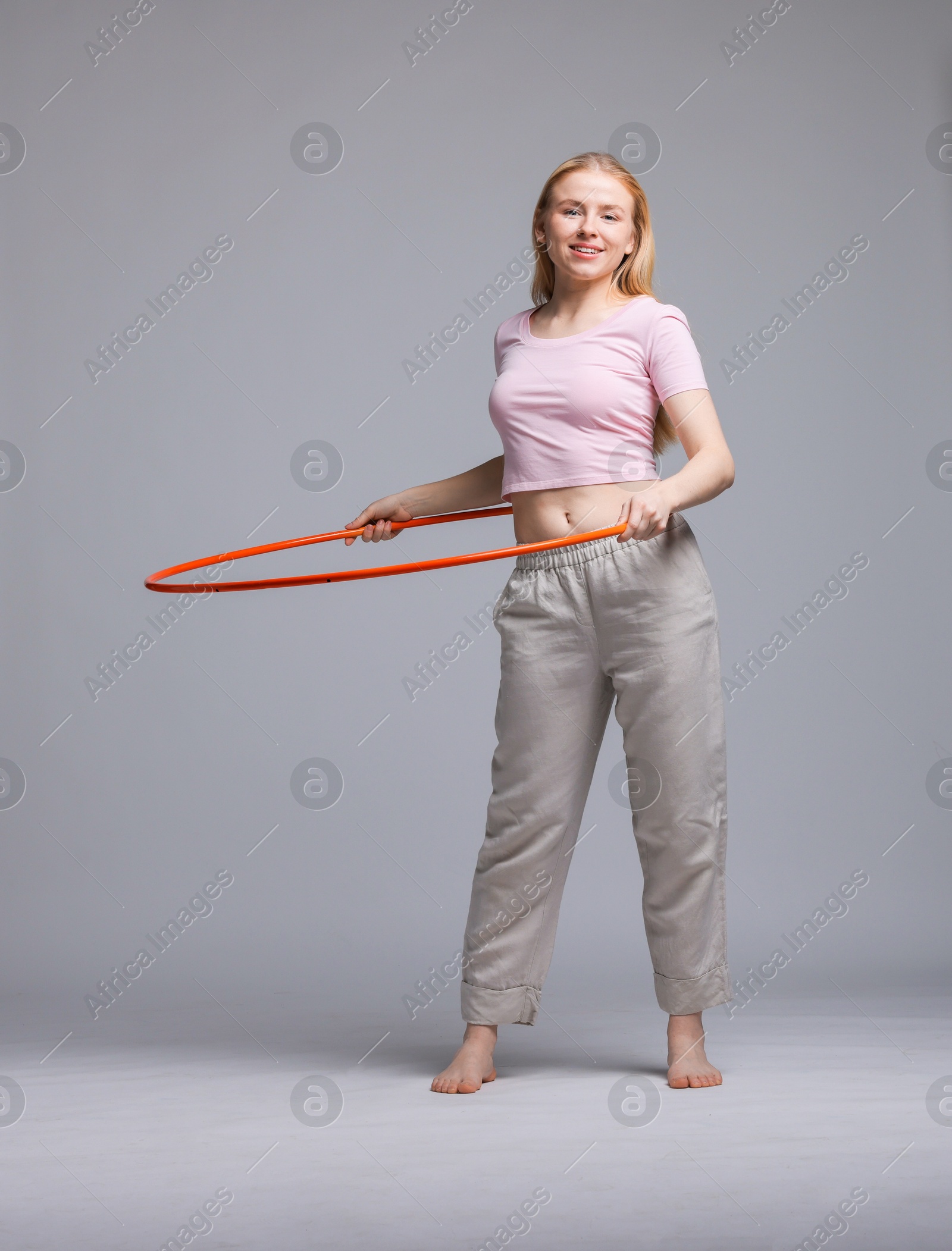 Photo of Beautiful young woman exercising with hula hoop on grey background