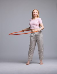 Photo of Beautiful young woman exercising with hula hoop on grey background