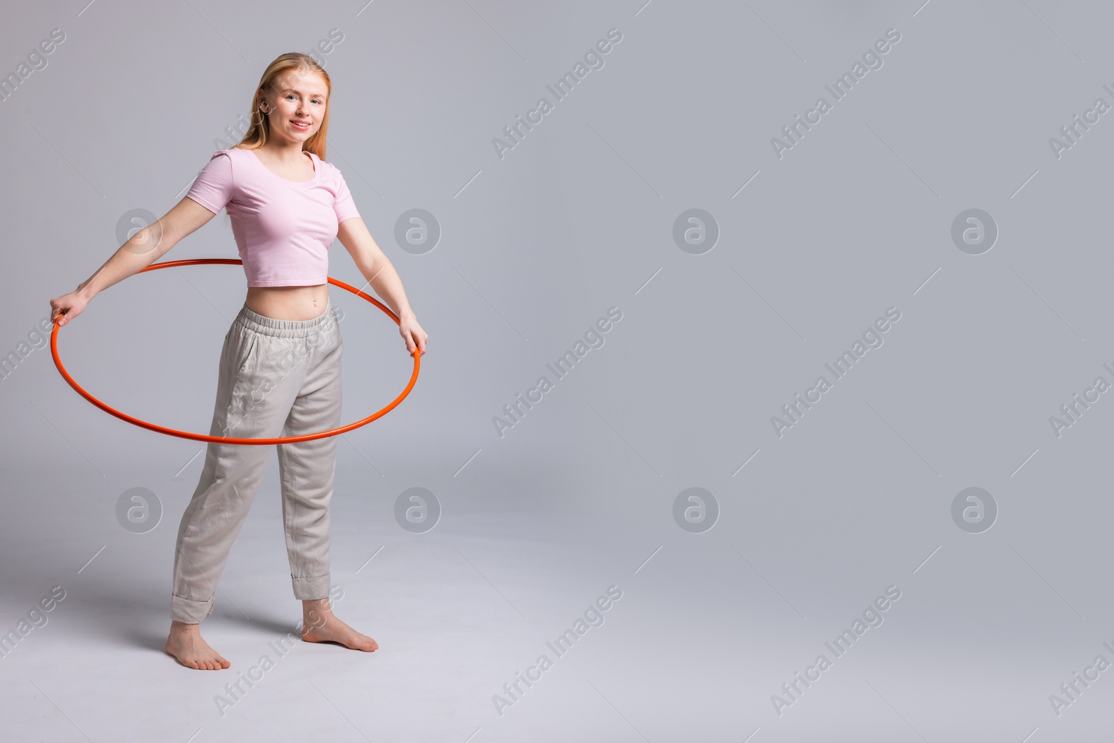 Photo of Beautiful young woman exercising with hula hoop on grey background, space for text