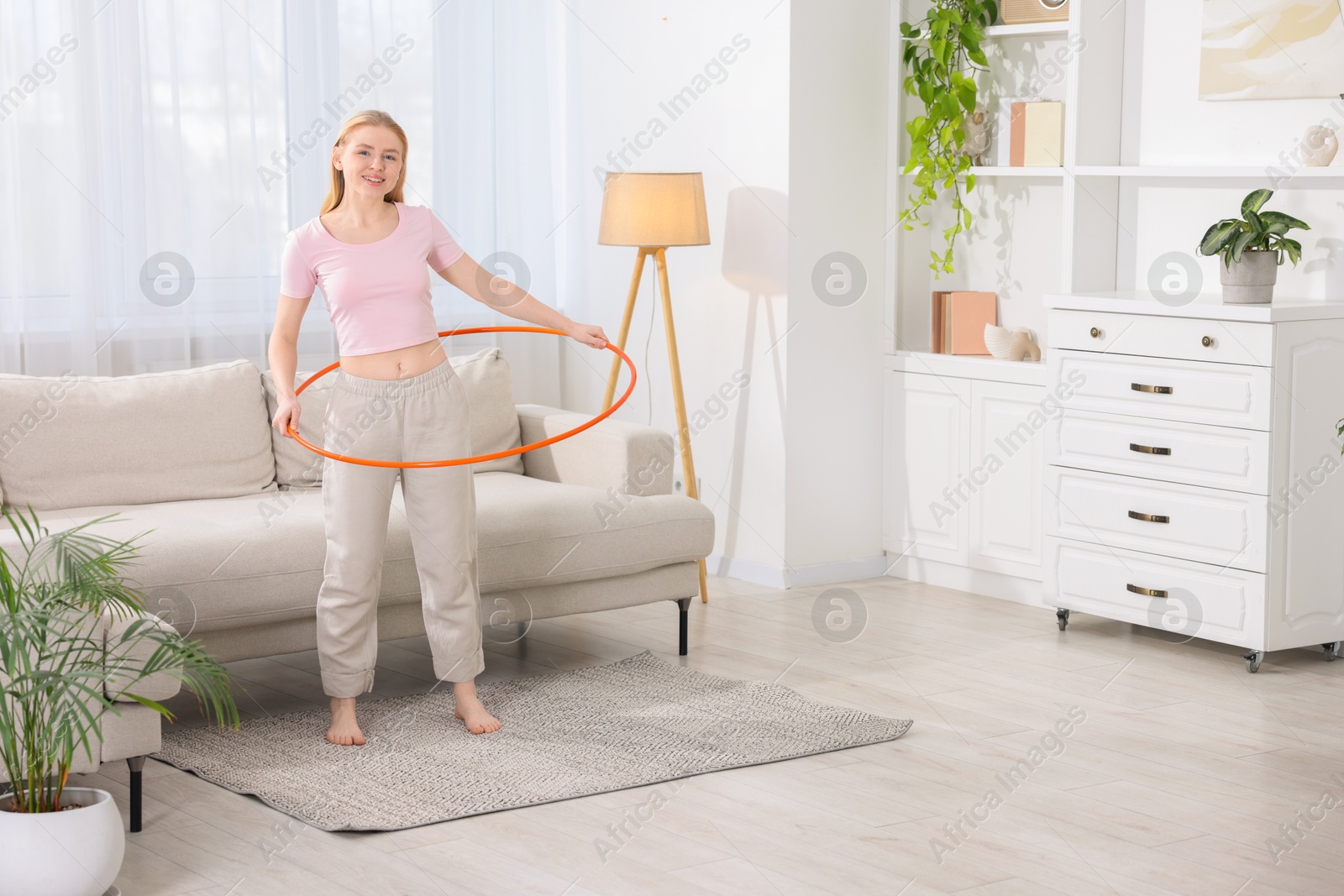 Photo of Beautiful young woman exercising with hula hoop at home