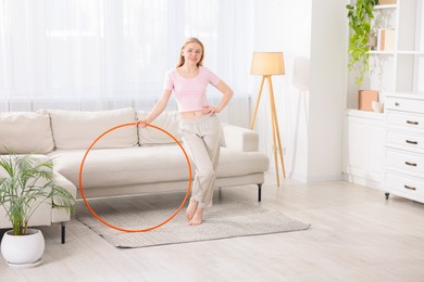 Photo of Beautiful young woman with hula hoop at home