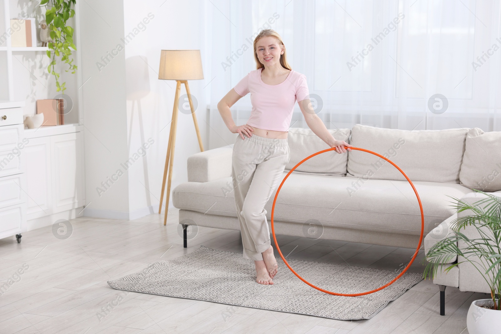 Photo of Beautiful young woman with hula hoop at home