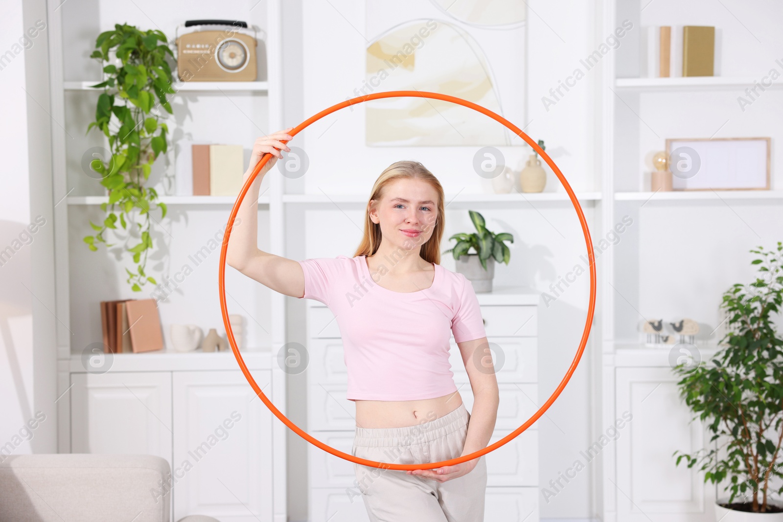 Photo of Beautiful young woman with hula hoop at home