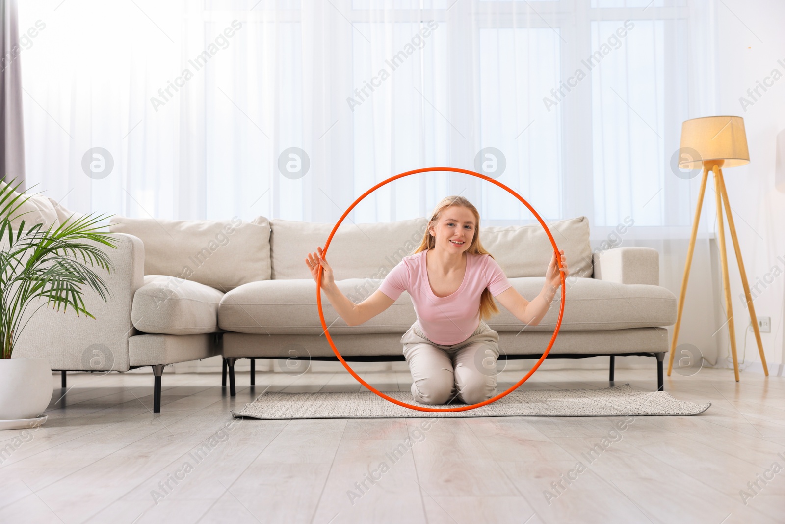 Photo of Beautiful young woman with hula hoop on floor at home