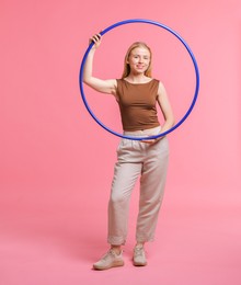 Beautiful young woman with hula hoop on pink background