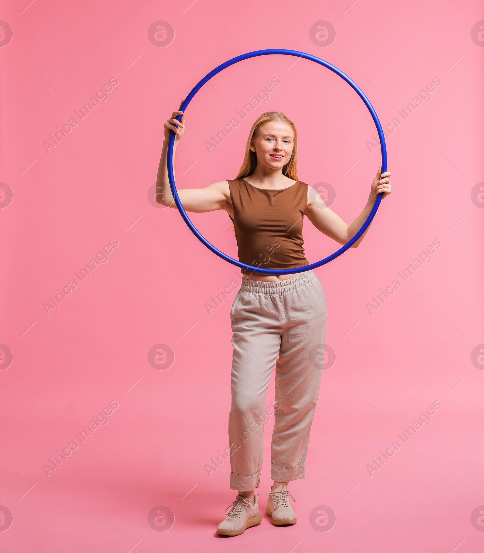 Photo of Beautiful young woman with hula hoop on pink background, space for text