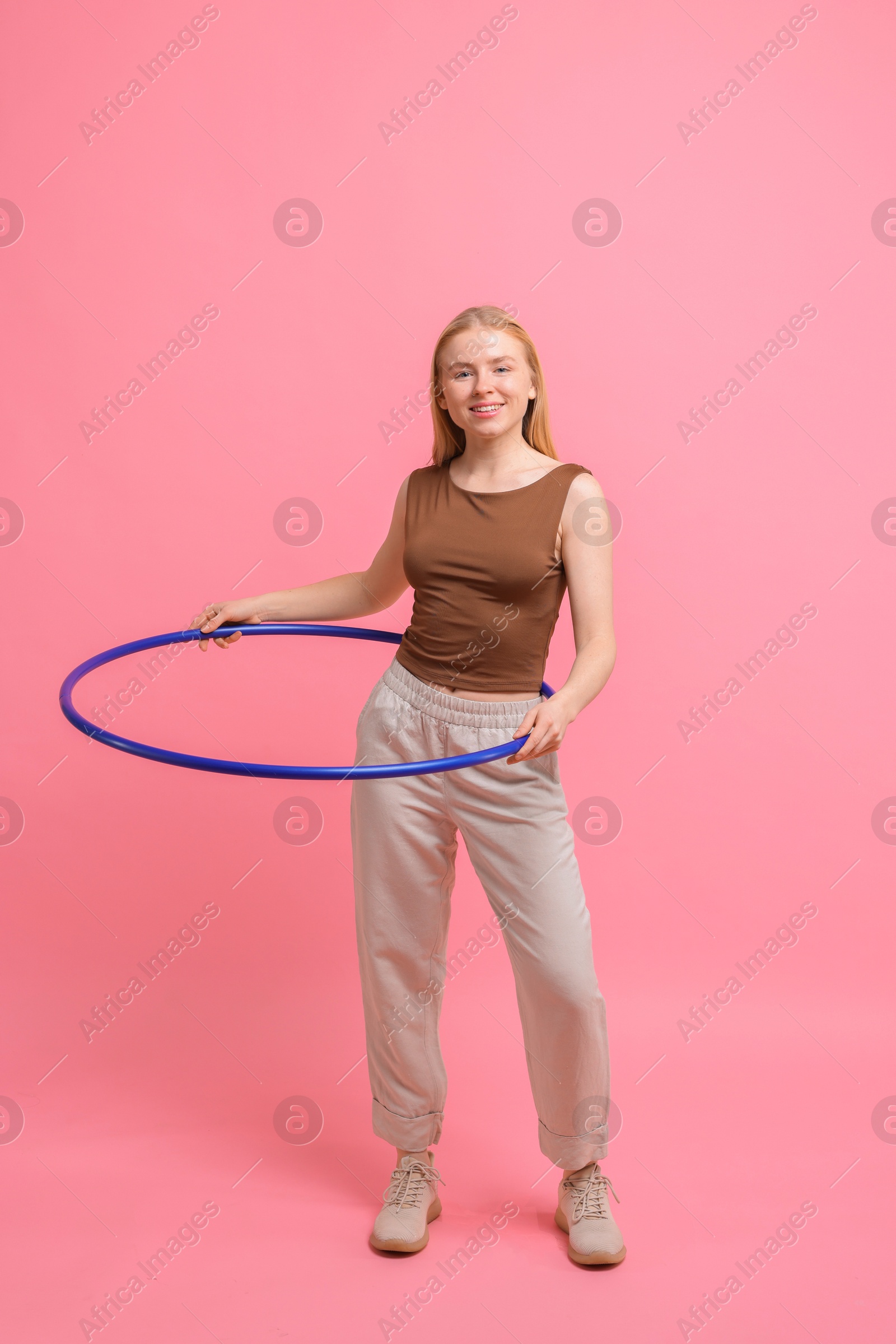 Photo of Beautiful young woman exercising with hula hoop on pink background