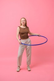 Beautiful young woman exercising with hula hoop on pink background