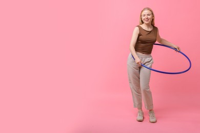 Photo of Beautiful young woman exercising with hula hoop on pink background, space for text