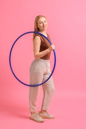 Beautiful young woman with hula hoop on pink background