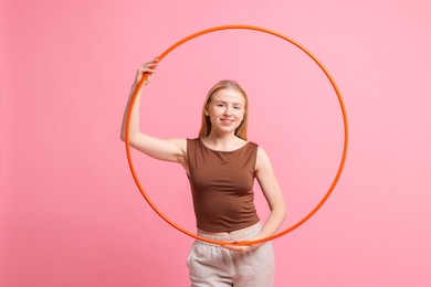 Beautiful young woman with hula hoop on pink background