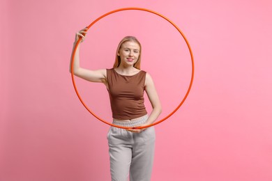 Beautiful young woman with hula hoop on pink background