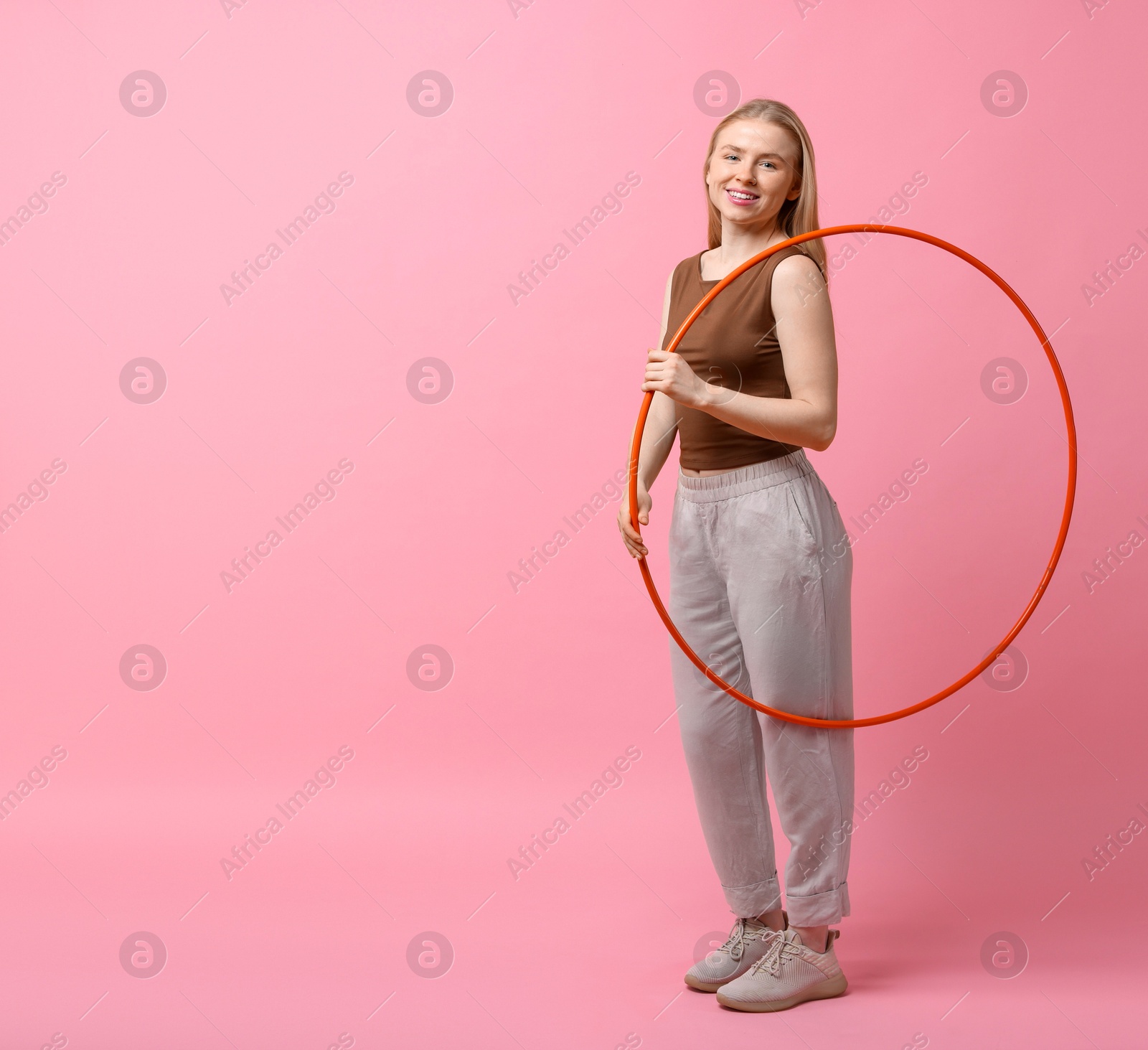 Photo of Beautiful young woman with hula hoop on pink background, space for text