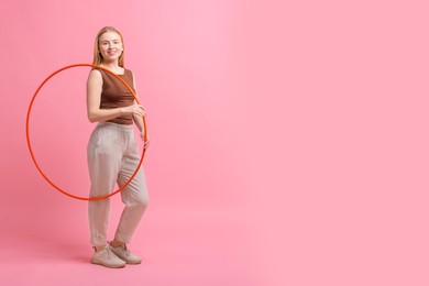 Photo of Beautiful young woman with hula hoop on pink background, space for text