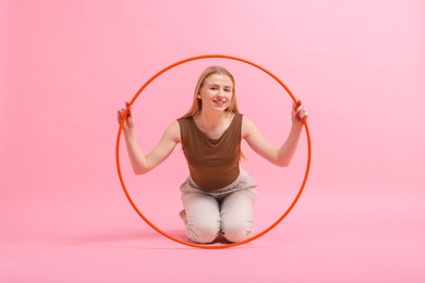 Beautiful young woman with hula hoop on pink background