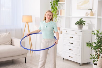 Beautiful young woman exercising with hula hoop at home