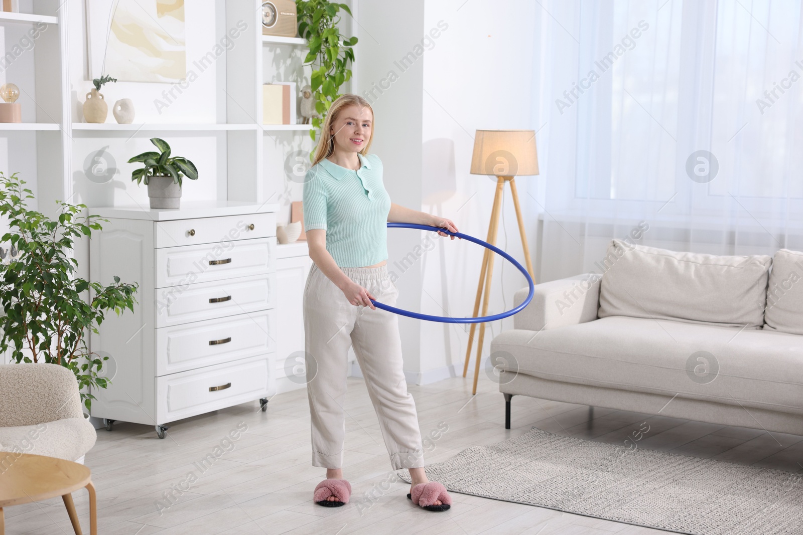 Photo of Beautiful young woman exercising with hula hoop at home