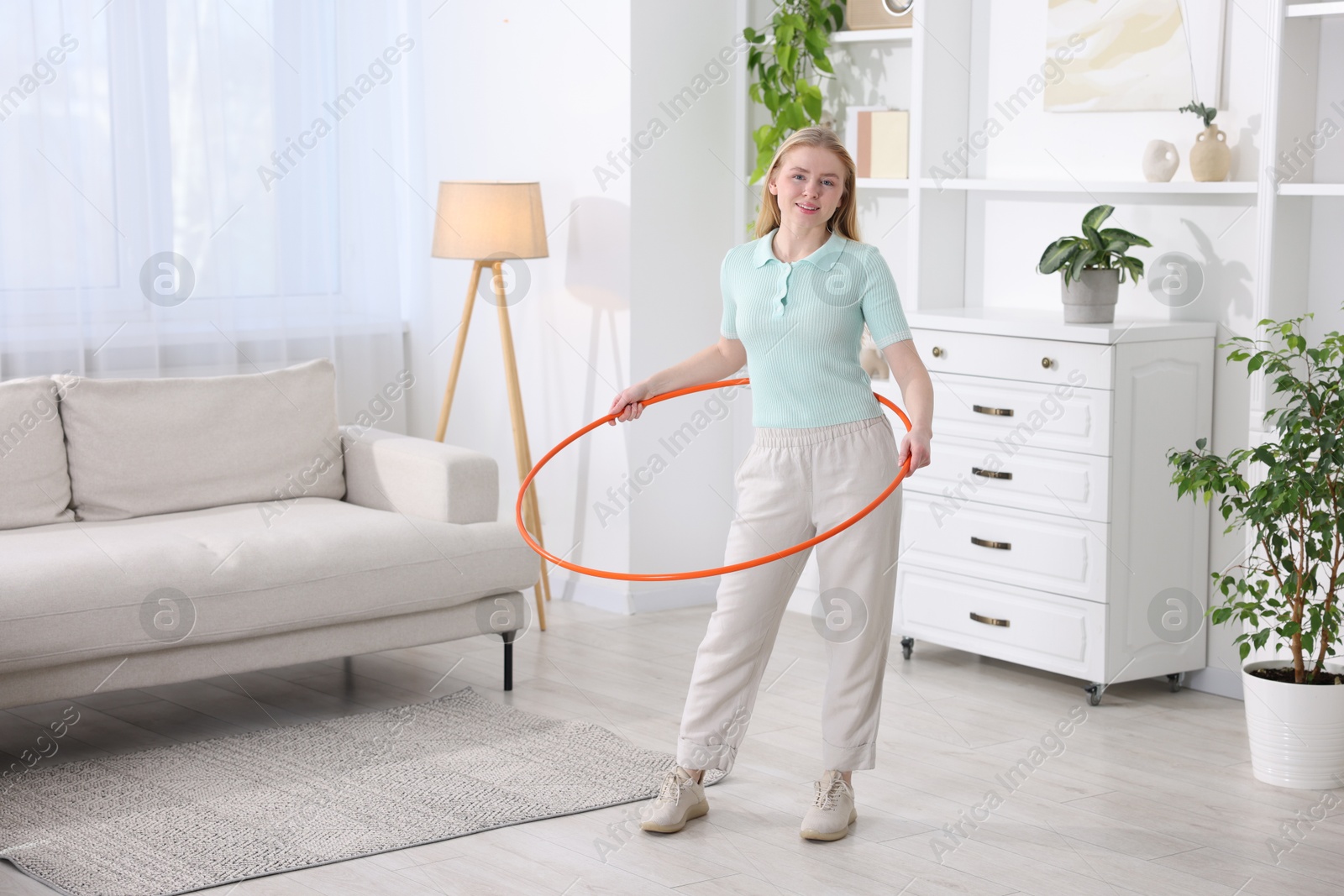 Photo of Beautiful young woman exercising with hula hoop at home