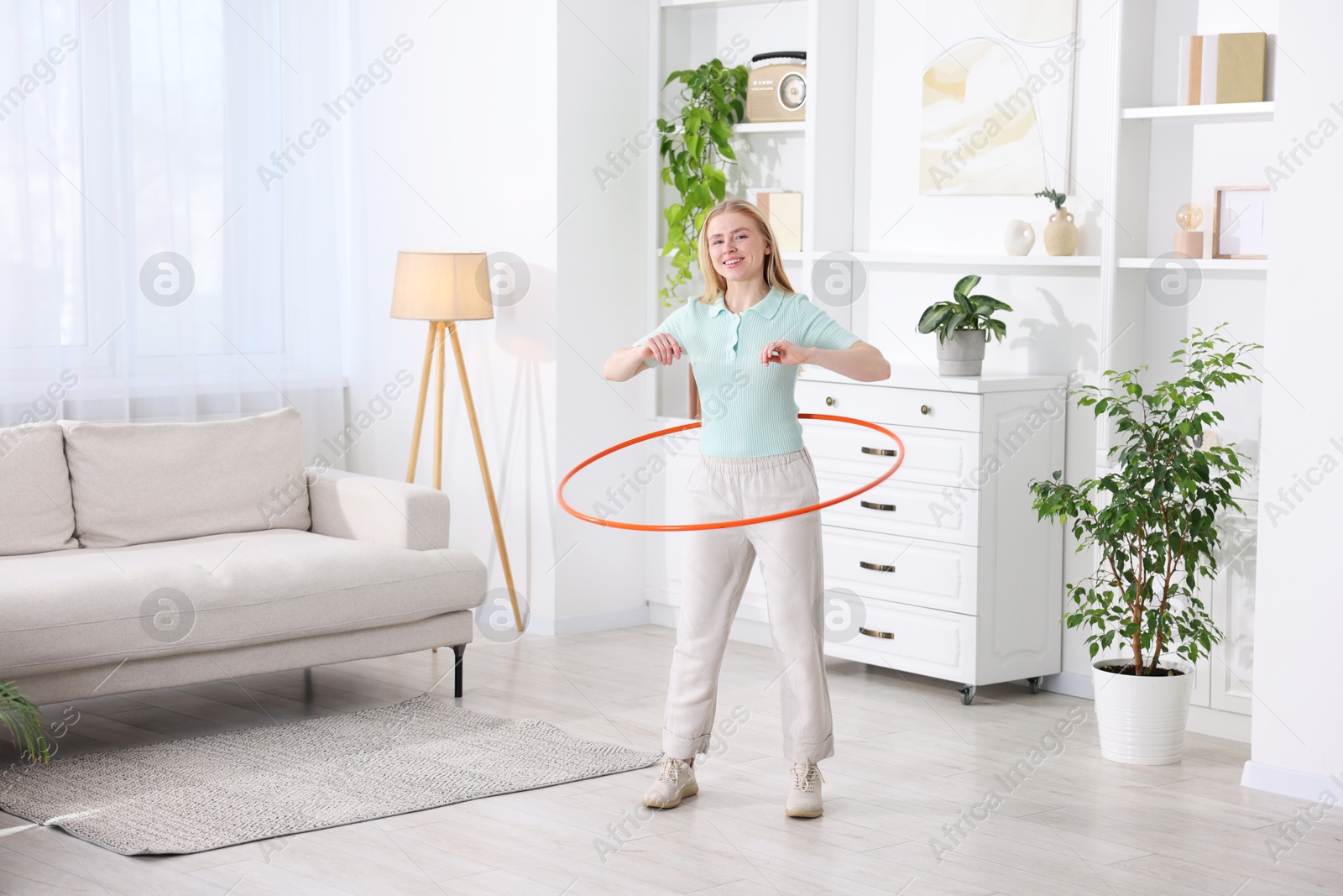 Photo of Beautiful young woman exercising with hula hoop at home