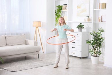 Beautiful young woman exercising with hula hoop at home