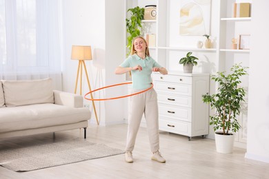 Photo of Beautiful young woman exercising with hula hoop at home