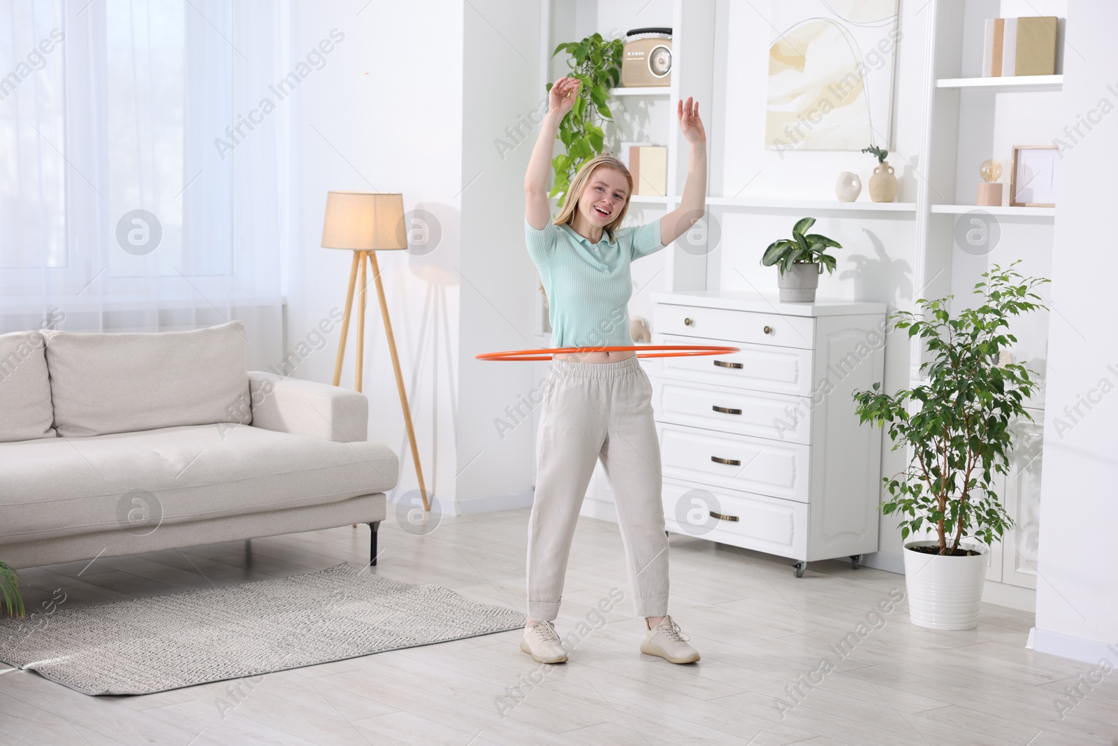 Photo of Beautiful young woman exercising with hula hoop at home