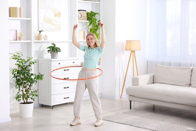 Photo of Beautiful young woman exercising with hula hoop at home