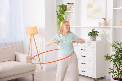 Photo of Beautiful young woman exercising with hula hoop at home