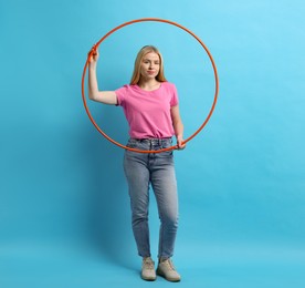 Photo of Beautiful young woman with hula hoop on light blue background