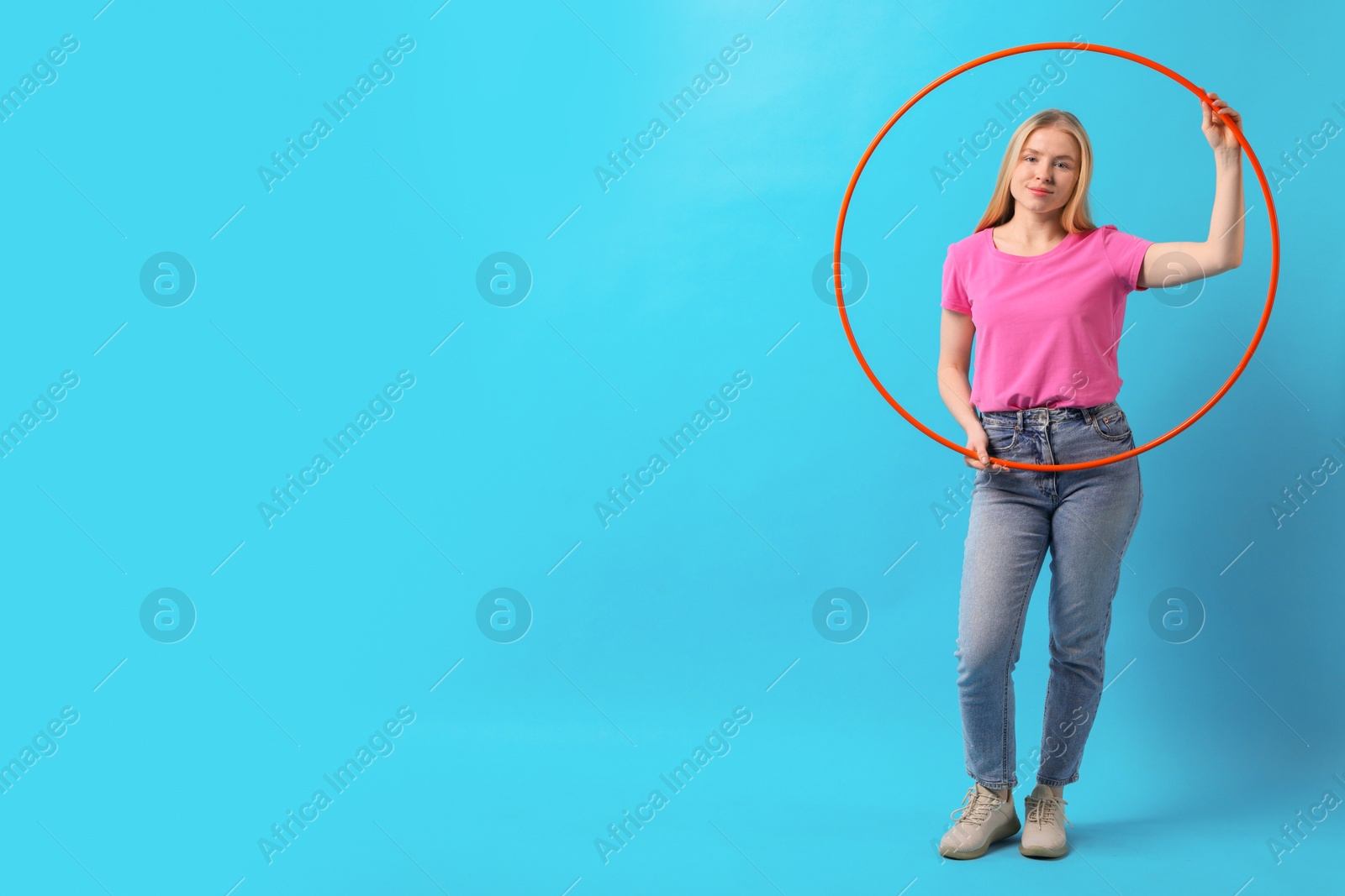 Photo of Beautiful young woman with hula hoop on light blue background, space for text