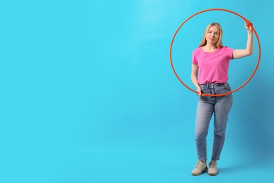 Beautiful young woman with hula hoop on light blue background, space for text