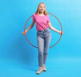 Beautiful young woman with hula hoop on light blue background