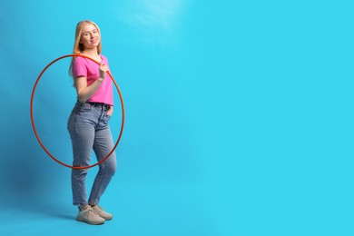 Photo of Beautiful young woman with hula hoop on light blue background, space for text