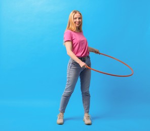 Beautiful young woman exercising with hula hoop on light blue background